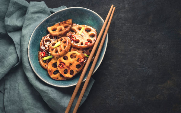Lotus root,or Renkon, or Rhizome stir-fry with spices, hot peppers, dark soy sauce and green onions with chopsticks on a dark rustic background, flat lay, copy space